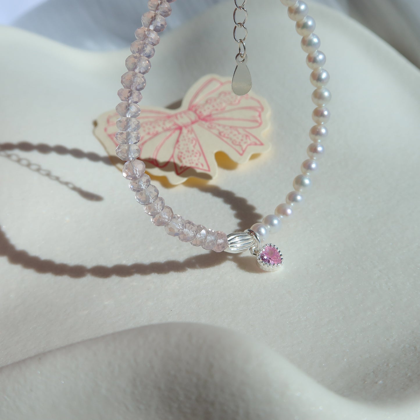 Pearl necklace with rose quartz gemstone and heart charm on a white surface