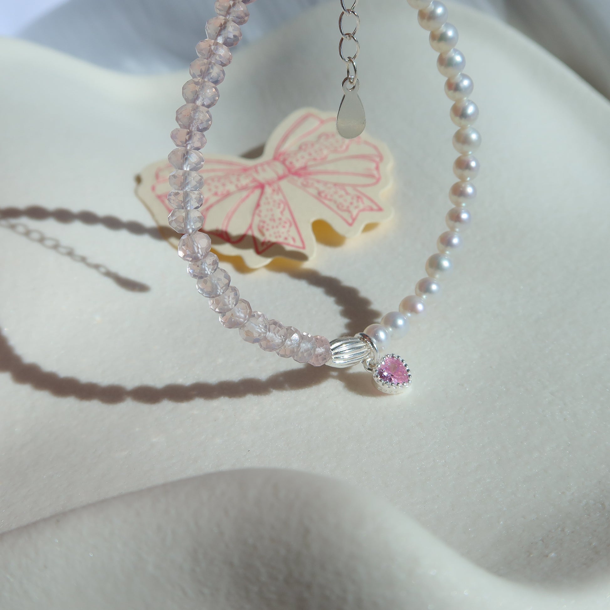 Pearl necklace with rose quartz gemstone and heart charm on a white surface