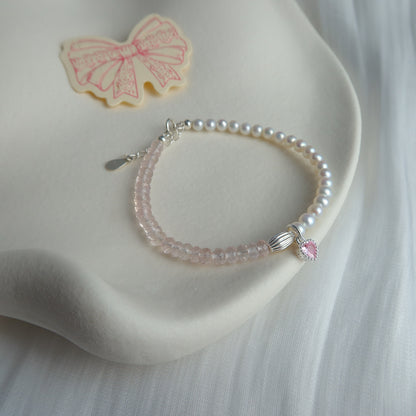 Pearl bracelet with a heart-shaped pink charm on a white surface