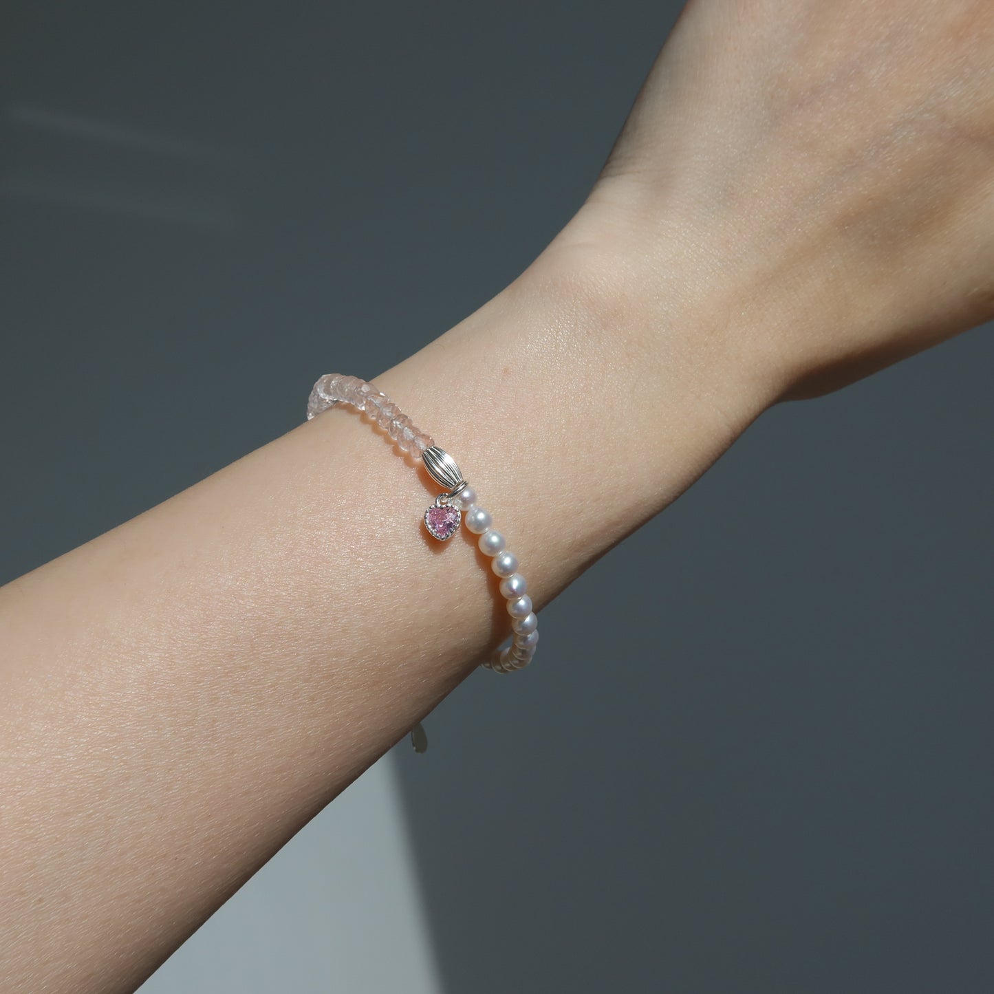 Pearl bracelet with a pink heart charm on a wrist against a dark background