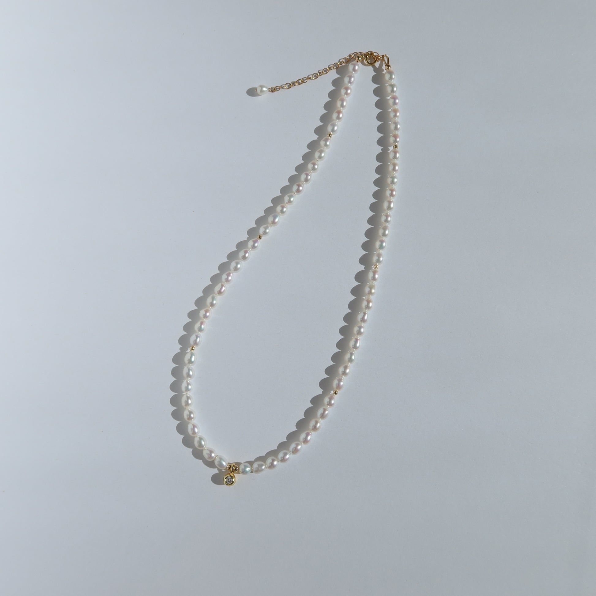 Pearl necklace with a gold clasp on a light gray background