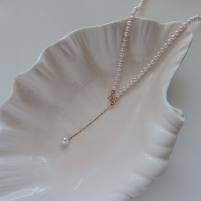 18k Gold Akoya Pearl Necklace resting on a white ceramic shell dish, highlighting its lustrous white Akoya pearls and delicate chain drop detail.