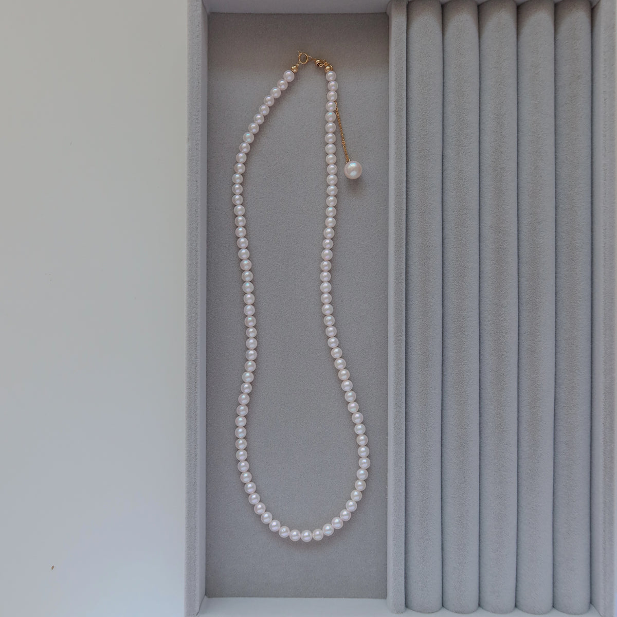 18k Gold Akoya Pearl Necklace displayed inside a gray velvet presentation box, highlighting its lustrous white Akoya pearls and delicate chain drop detail.