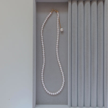 18k Gold Akoya Pearl Necklace displayed inside a gray velvet presentation box, highlighting its lustrous white Akoya pearls and delicate chain drop detail.