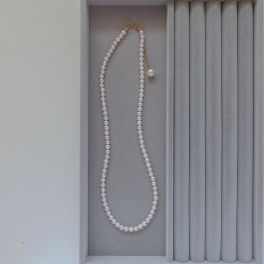 18k Gold Akoya Pearl Necklace displayed inside a gray velvet presentation box, highlighting its lustrous white Akoya pearls and delicate chain drop detail.