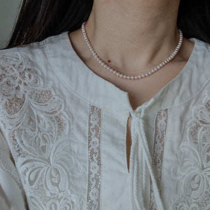 Close-up of a person wearing the 18k Gold Akoya Pearl Necklace, highlighting its lustrous white Akoya pearls and delicate chain drop detail against a white lace top.