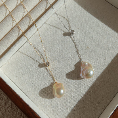 Two baroque pearl necklaces, one gold and one silver, displayed on a cream-colored jewelry box.