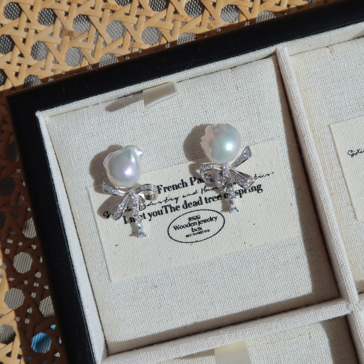 Coquette Baroque Pearl Earrings displayed inside a presentation box on a vintage-style card, highlighting their white baroque pearls and sparkling pavé ribbon bow studs.