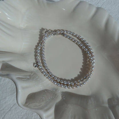 Blue Akoya Pearl Necklace coiled on a white ceramic shell dish in soft natural light, highlighting its lustrous blue Akoya pearls and delicate chain detail.