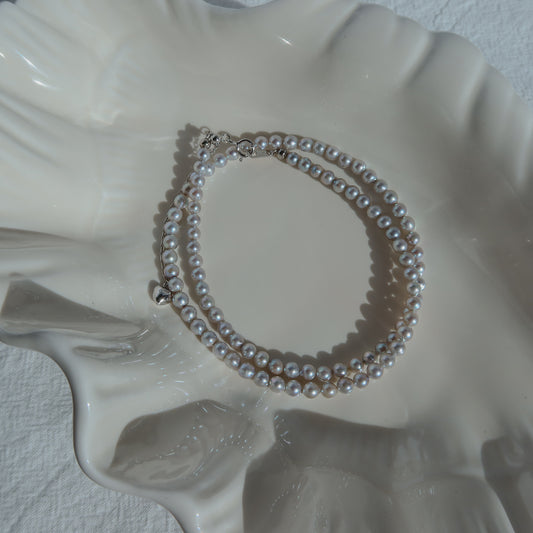 Blue Akoya Pearl Necklace coiled on a white ceramic shell dish in soft natural light, highlighting its lustrous blue Akoya pearls and delicate chain detail.