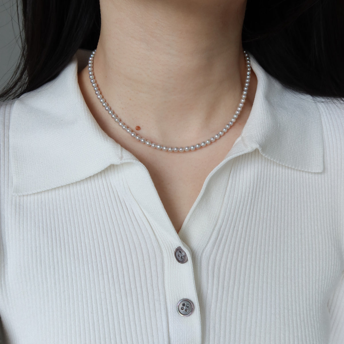 Close-up of a person wearing the Blue Akoya Pearl Necklace, highlighting its lustrous blue Akoya pearls and delicate chain detail against a white polo top.