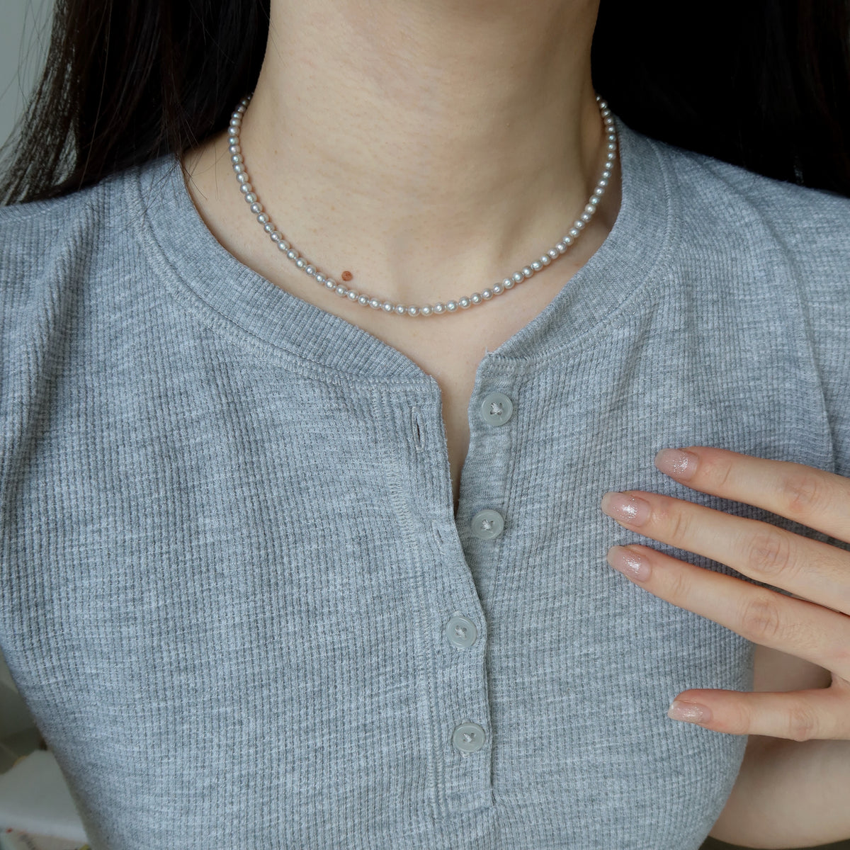 Close-up of a person wearing the Blue Akoya Pearl Necklace, highlighting its lustrous blue Akoya pearls and delicate chain detail against a gray ribbed top.
