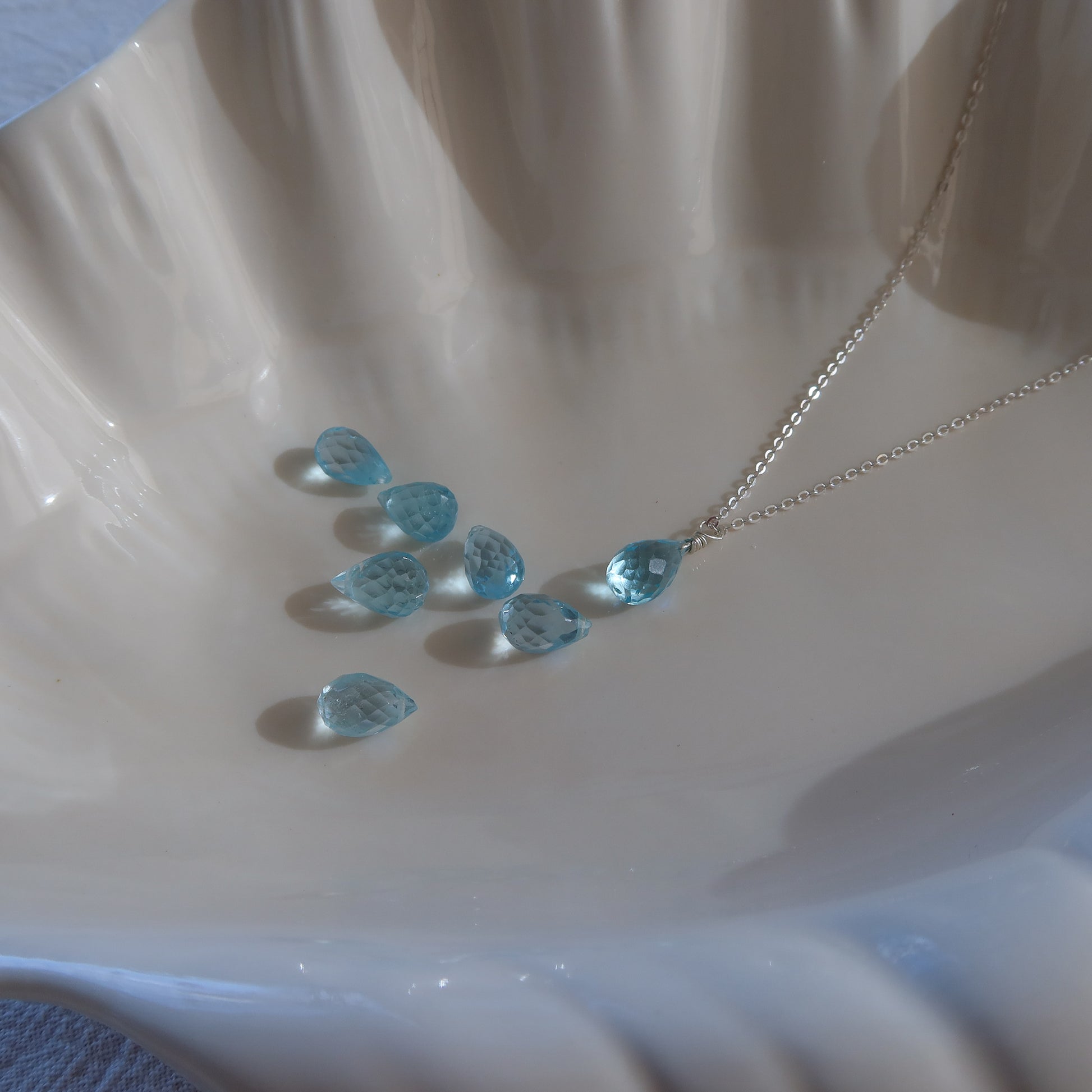 Necklace with blue teardrop-shaped topaz on a white shell background