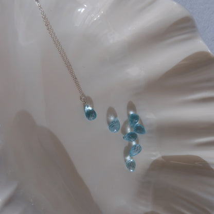 Necklace with blue teardrop topaz pendant on a white shell background