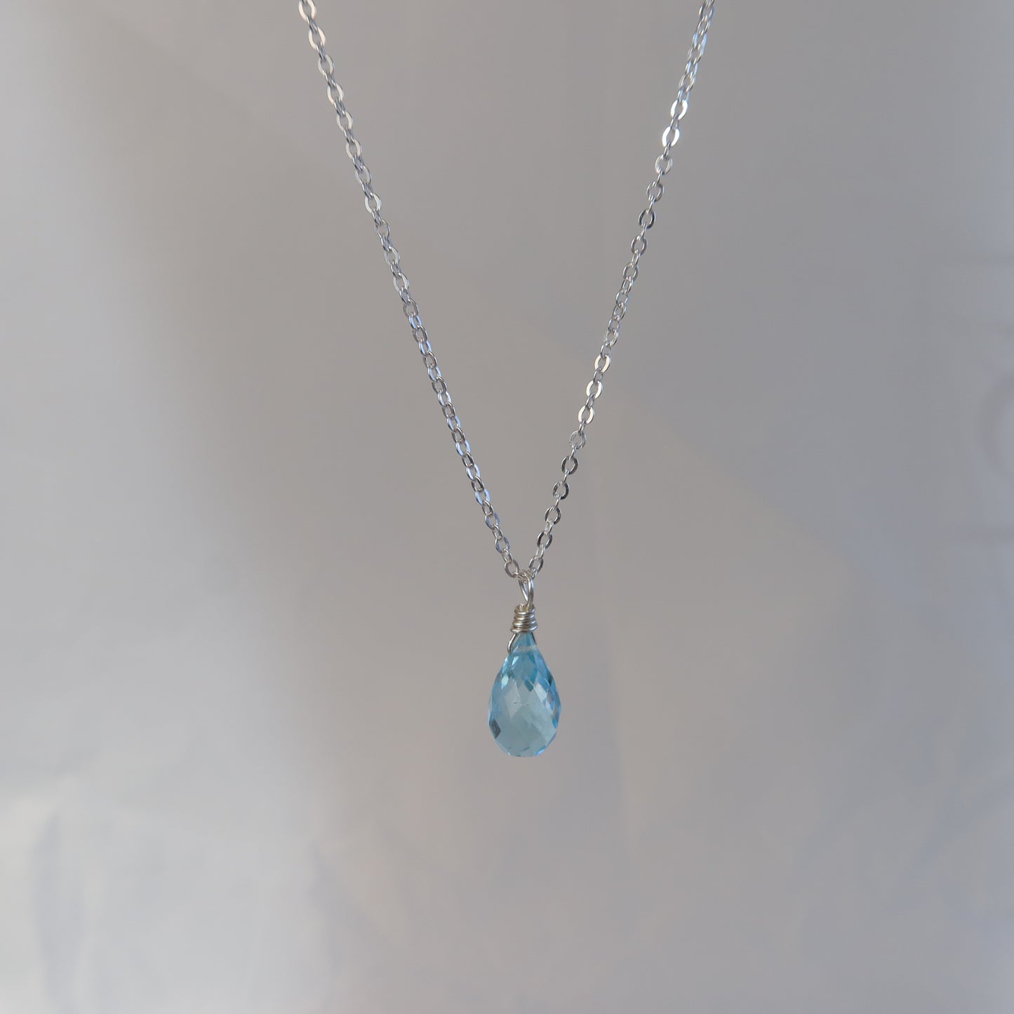 Necklace with a blue teardrop topaz on a plain background