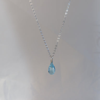 Necklace with a blue teardrop topaz on a plain background