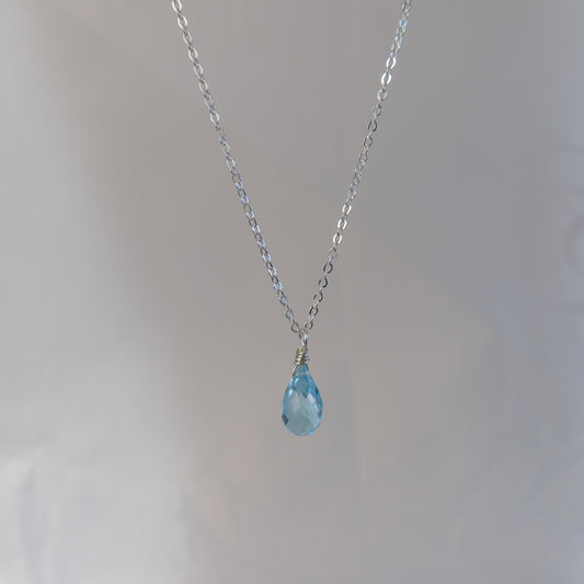 Necklace with a blue teardrop topaz on a plain background