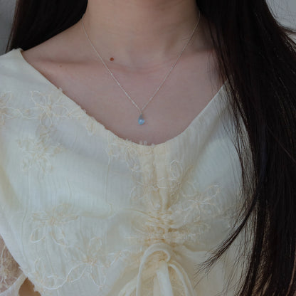 Close-up of a person wearing a delicate blue topaz necklace with a light-colored top.