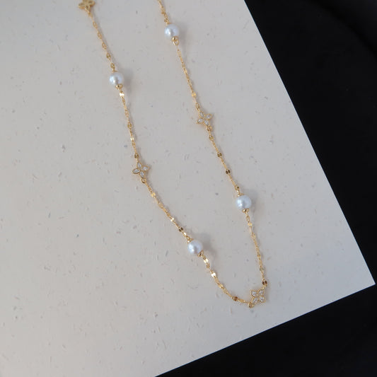 A delicate gold chain necklace featuring small white pearl beads and tiny gold star charms, laid out on a white textured surface with a black background visible in the corner.