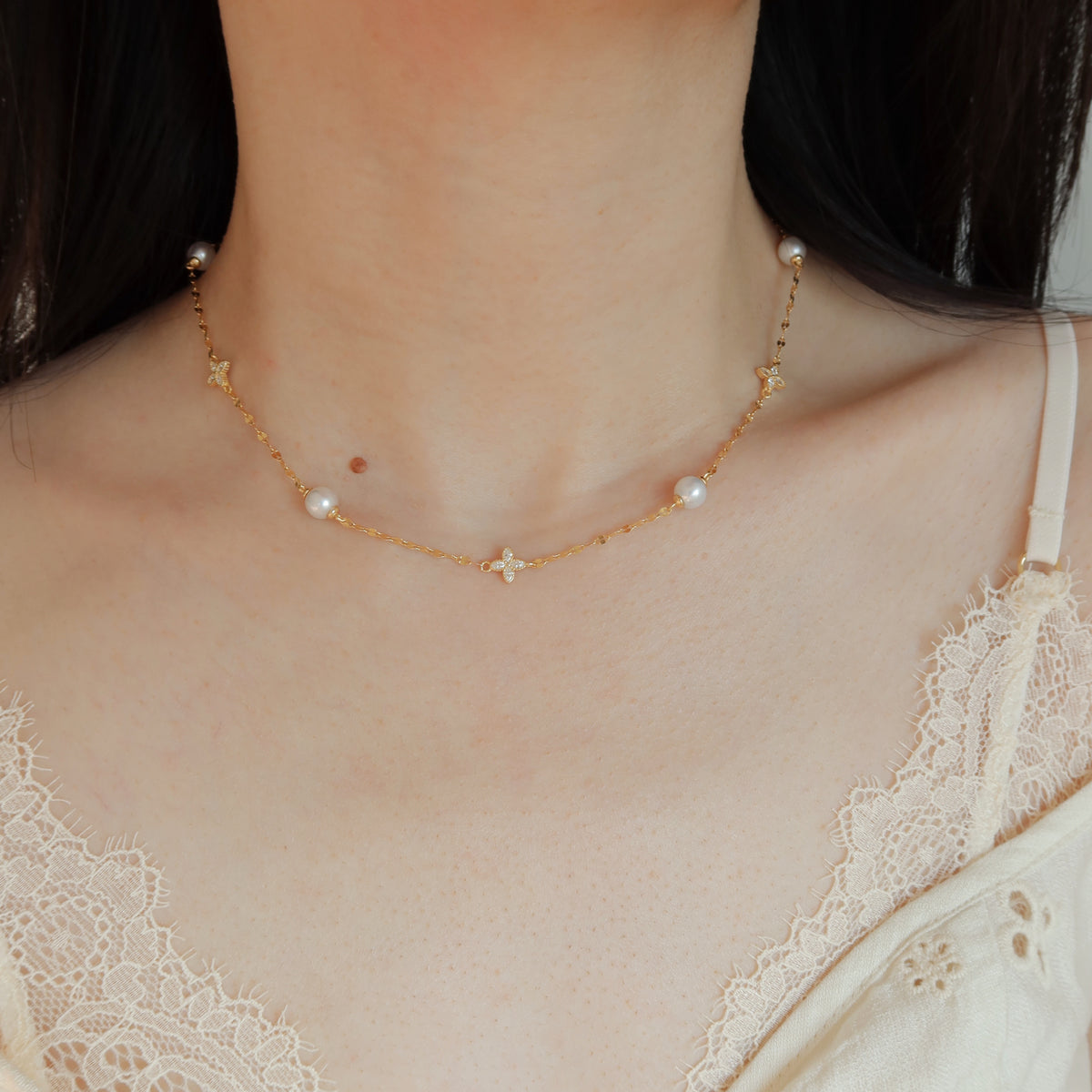 A delicate gold chain necklace with small freshwater pearl beads and clover motifs, worn by a model in a close-up shot.