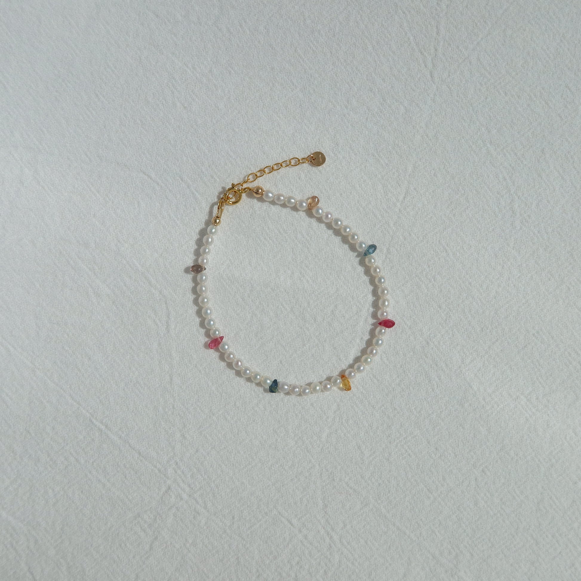 Pearl bracelet withrainbow sapphire beads on a light gray background