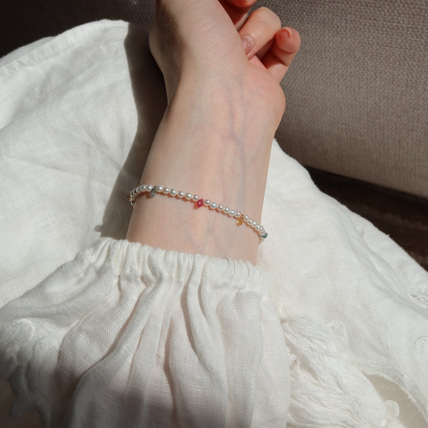 Close-up of a wrist wearing a bracelet with small sapphire beads on a white fabric background