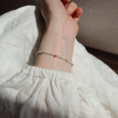 Close-up of a wrist wearing a bracelet with small sapphire beads on a white fabric background