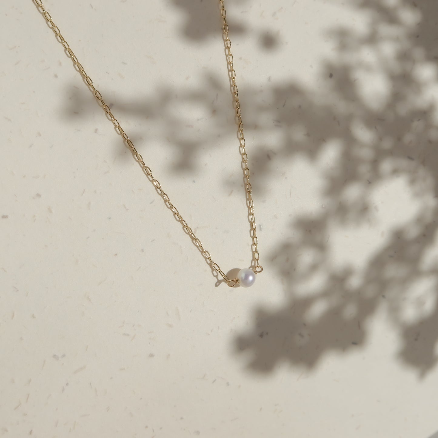 Gold necklace with a pearl pendant on a light beige background