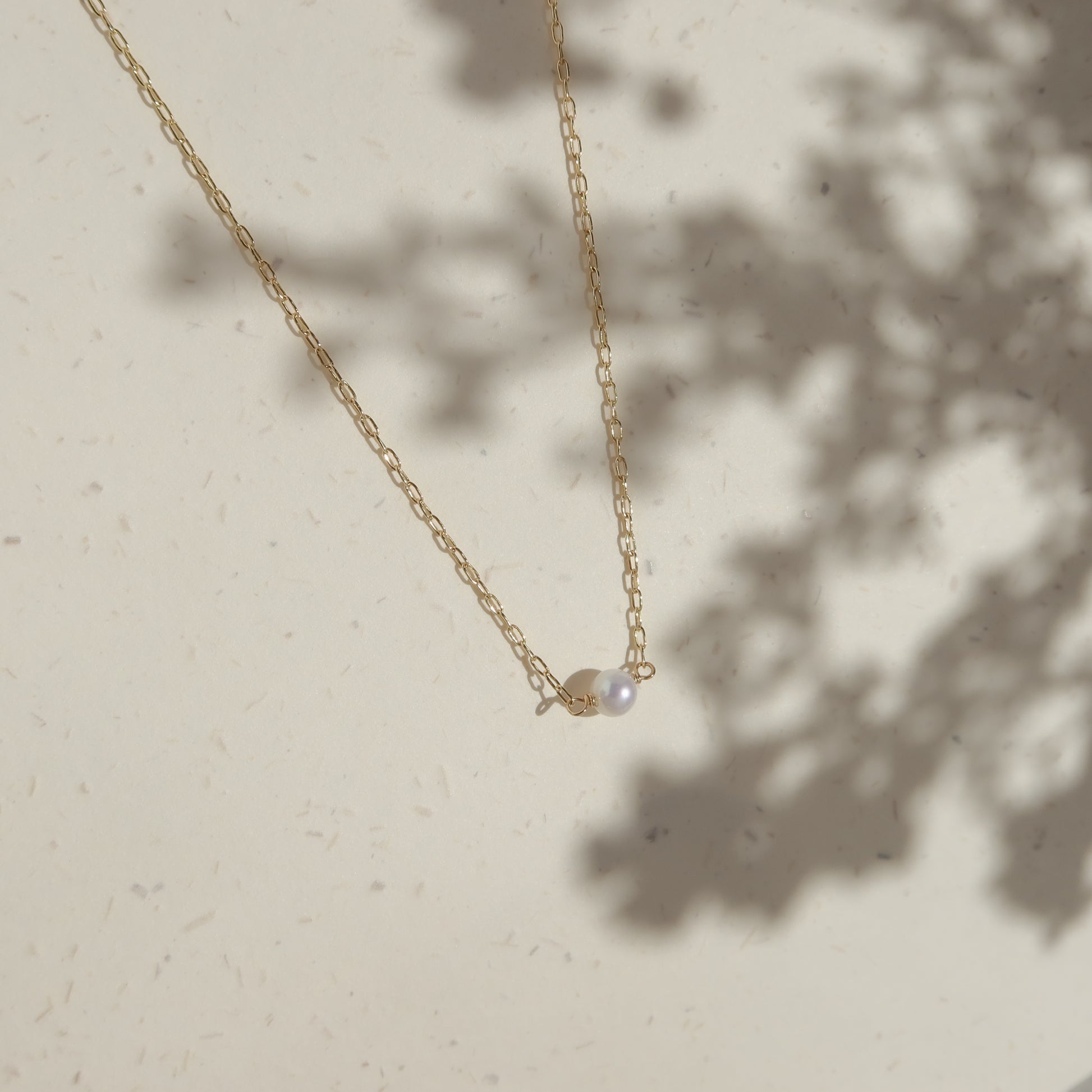 Gold necklace with a pearl pendant on a light beige background