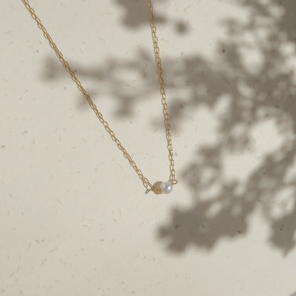 Gold necklace with a pearl pendant on a light beige background