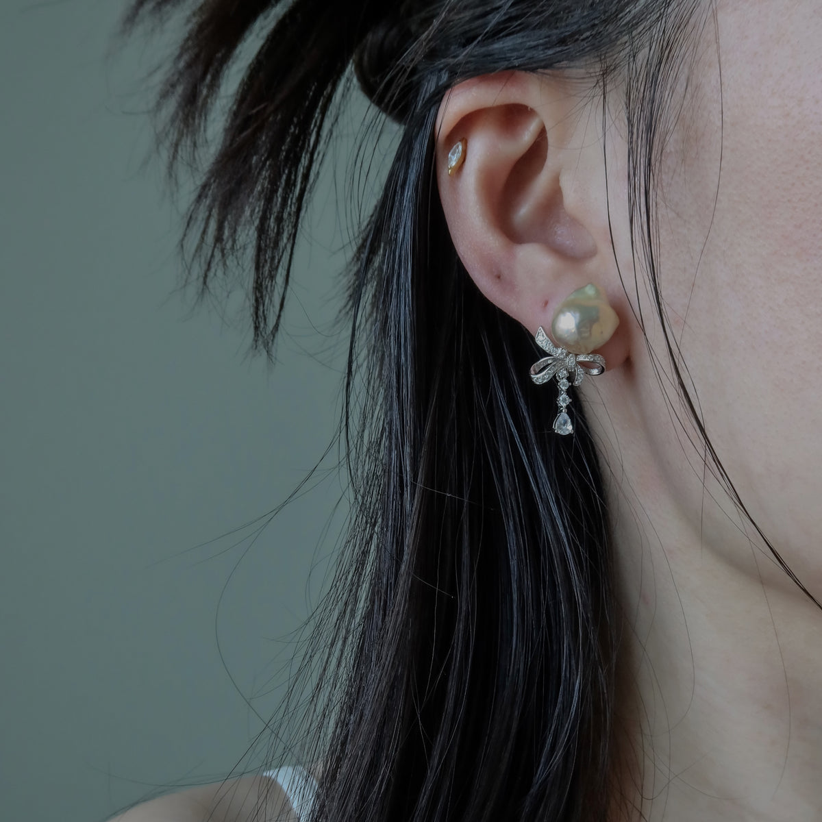 Close-up of a person wearing the Coquette Baroque Pearl Earrings, highlighting their pink-toned baroque pearl and sparkling pavé ribbon bow design.