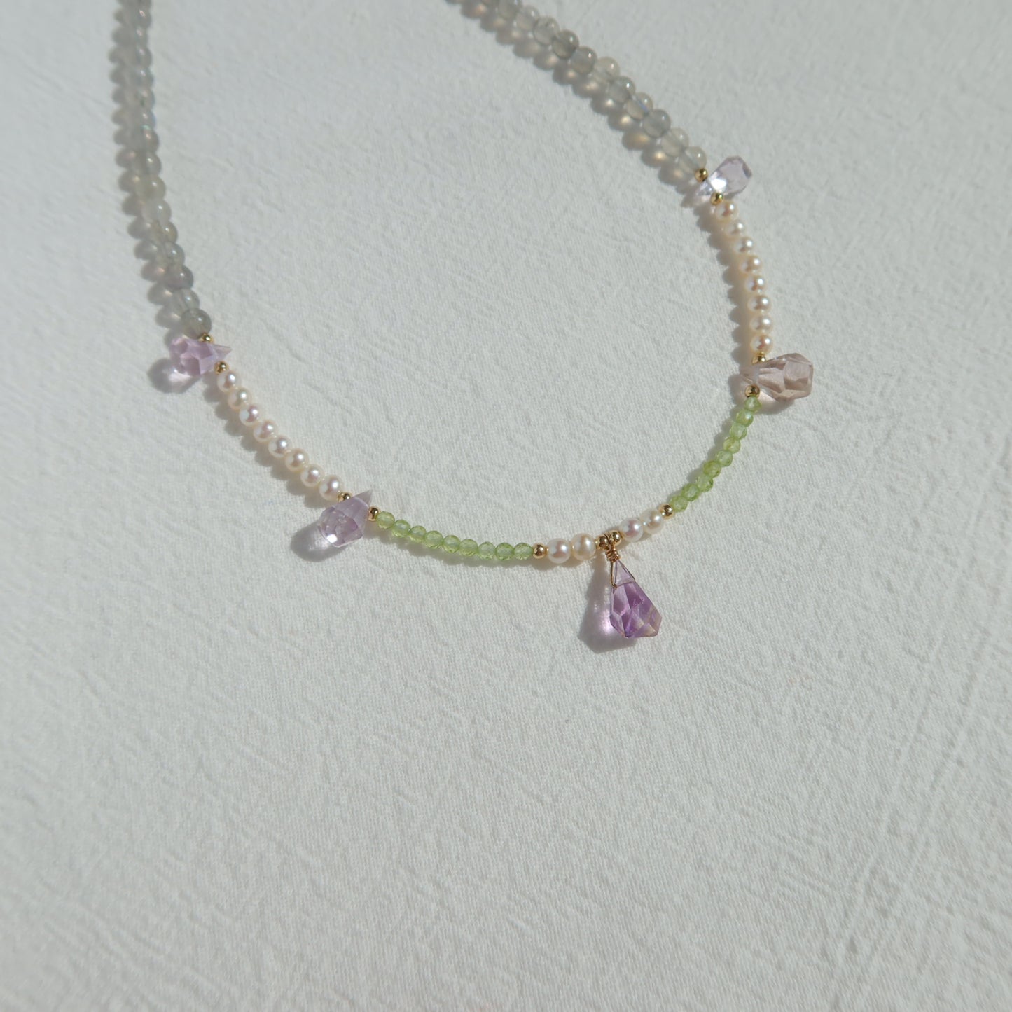 Necklace with pearls, moonstone and ametrine stones on a light gray background