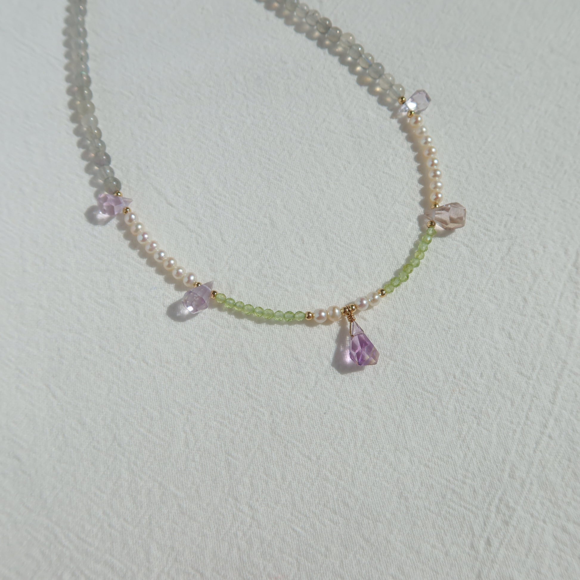 Necklace with pearls, moonstone and ametrine stones on a light gray background