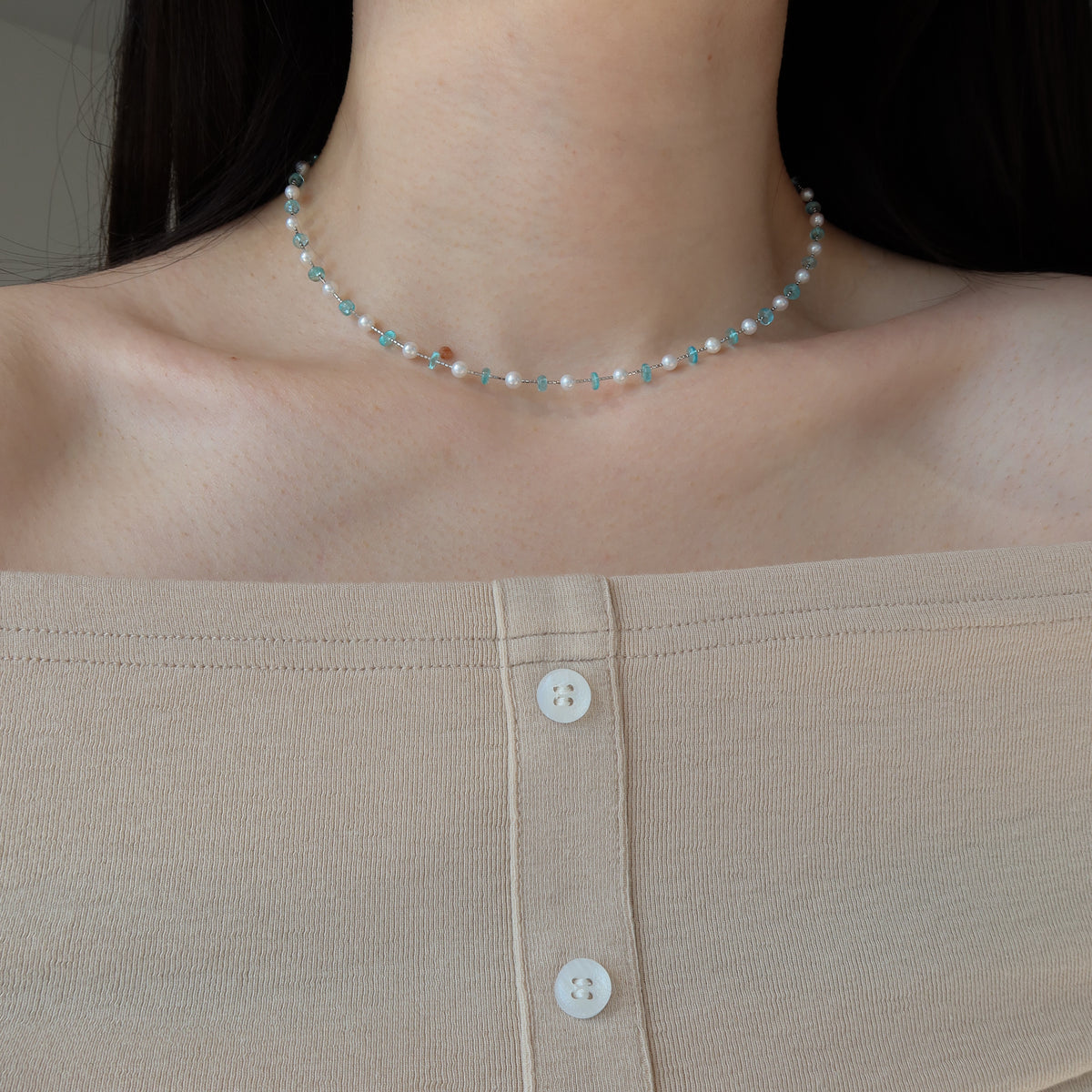 A close-up of a person's neck and upper chest wearing a delicate beaded choker necklace. The necklace features small white pearl beads with light blue apatite crystals.