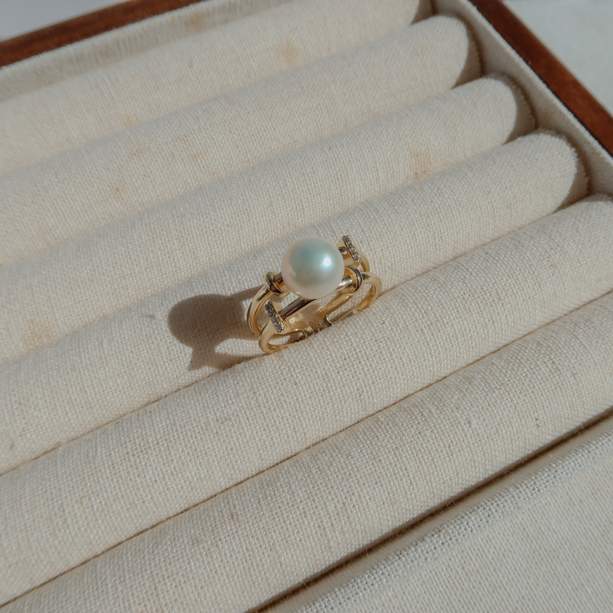 A gold ring with a single white pearl, displayed on the cream-colored padded slots of a jewelry box.