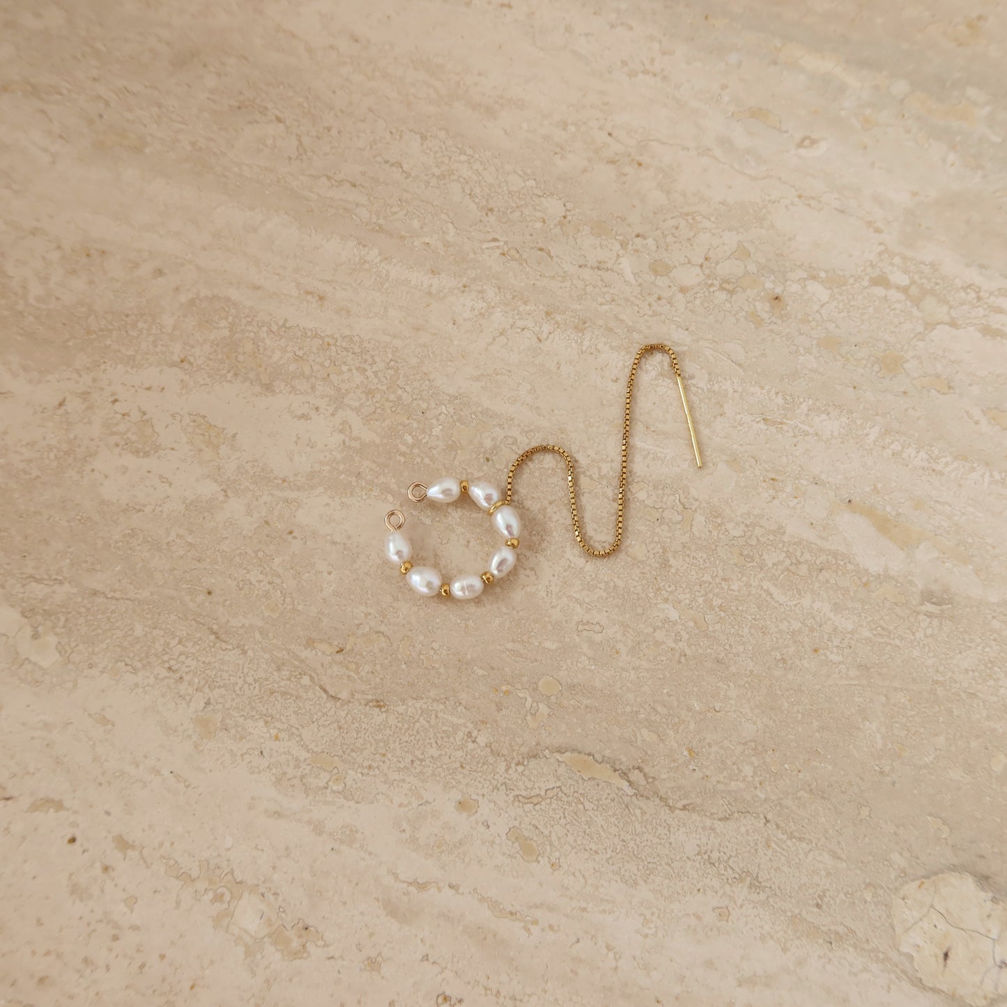 Gold ear cuff with pearl beads on a beige stone surface