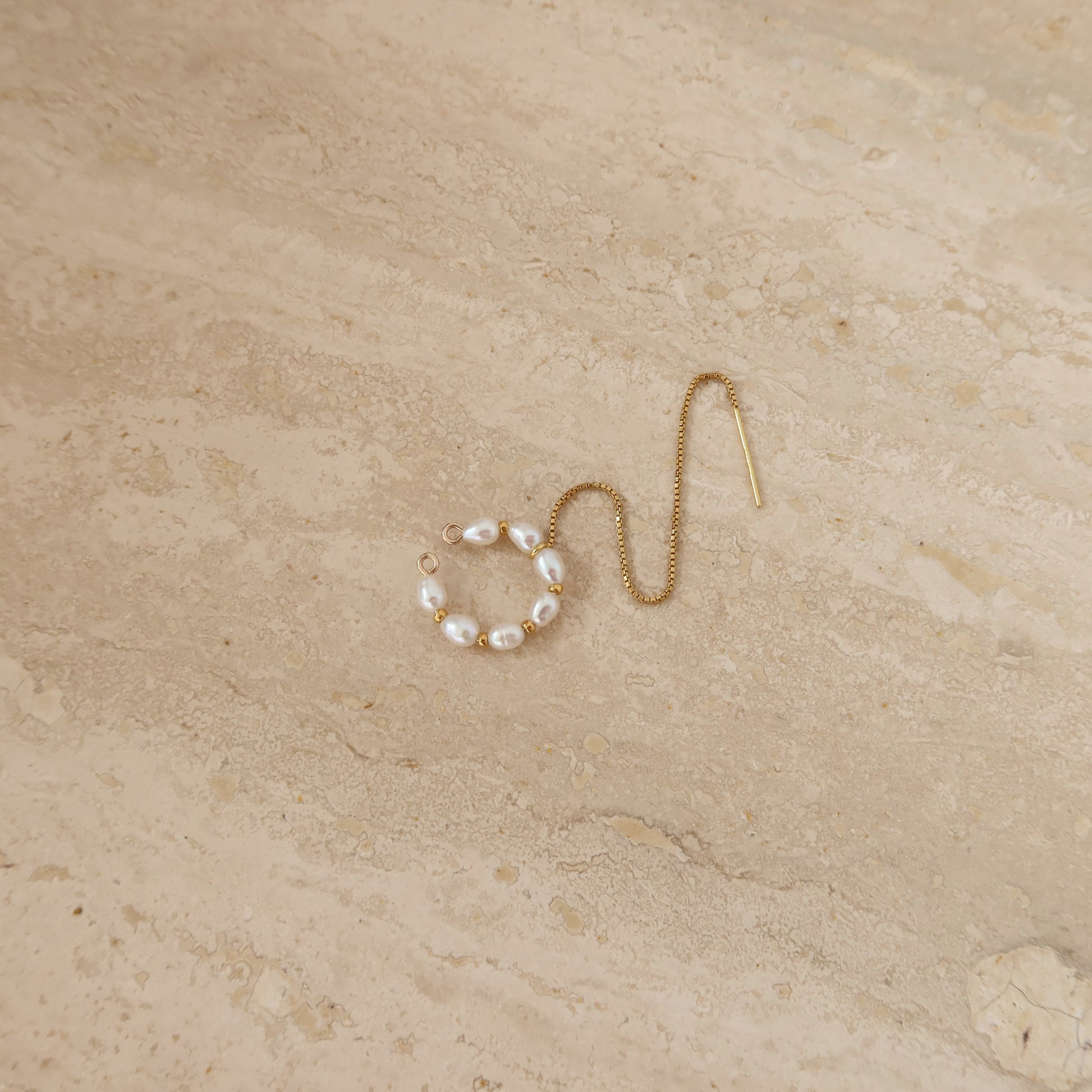Gold ear cuff with pearl beads on a beige stone surface