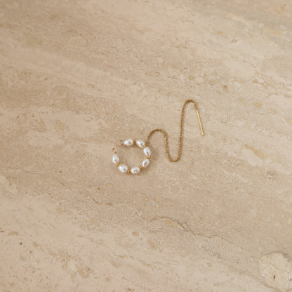 Gold ear cuff with pearl beads on a beige stone surface