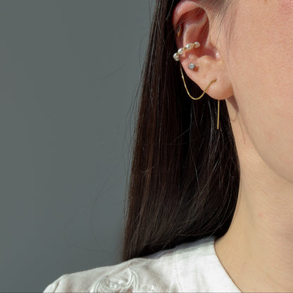 Close-up of an ear with a pearl ear cuff with gold threader against a gray background