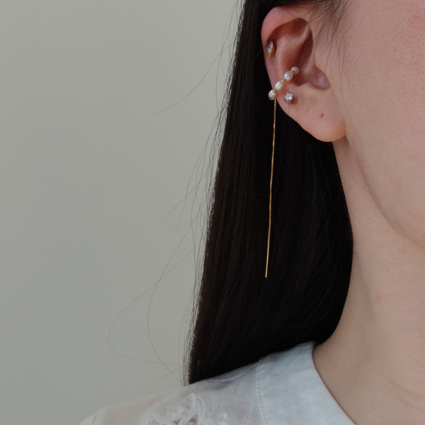 Close-up of an ear wearing a delicate earring with pearls against a neutral background