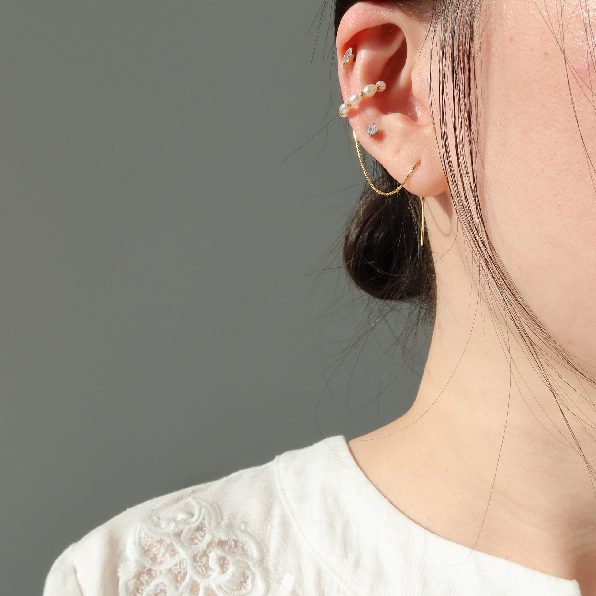 Close-up of a person wearing gold pearl ear cuff with a neutral background
