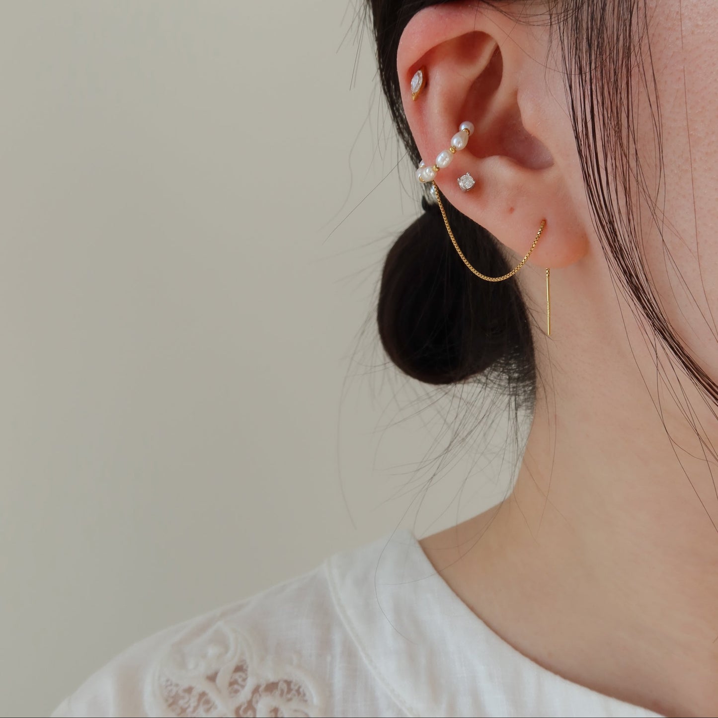 Close-up of an ear with pearl earrings against a neutral background