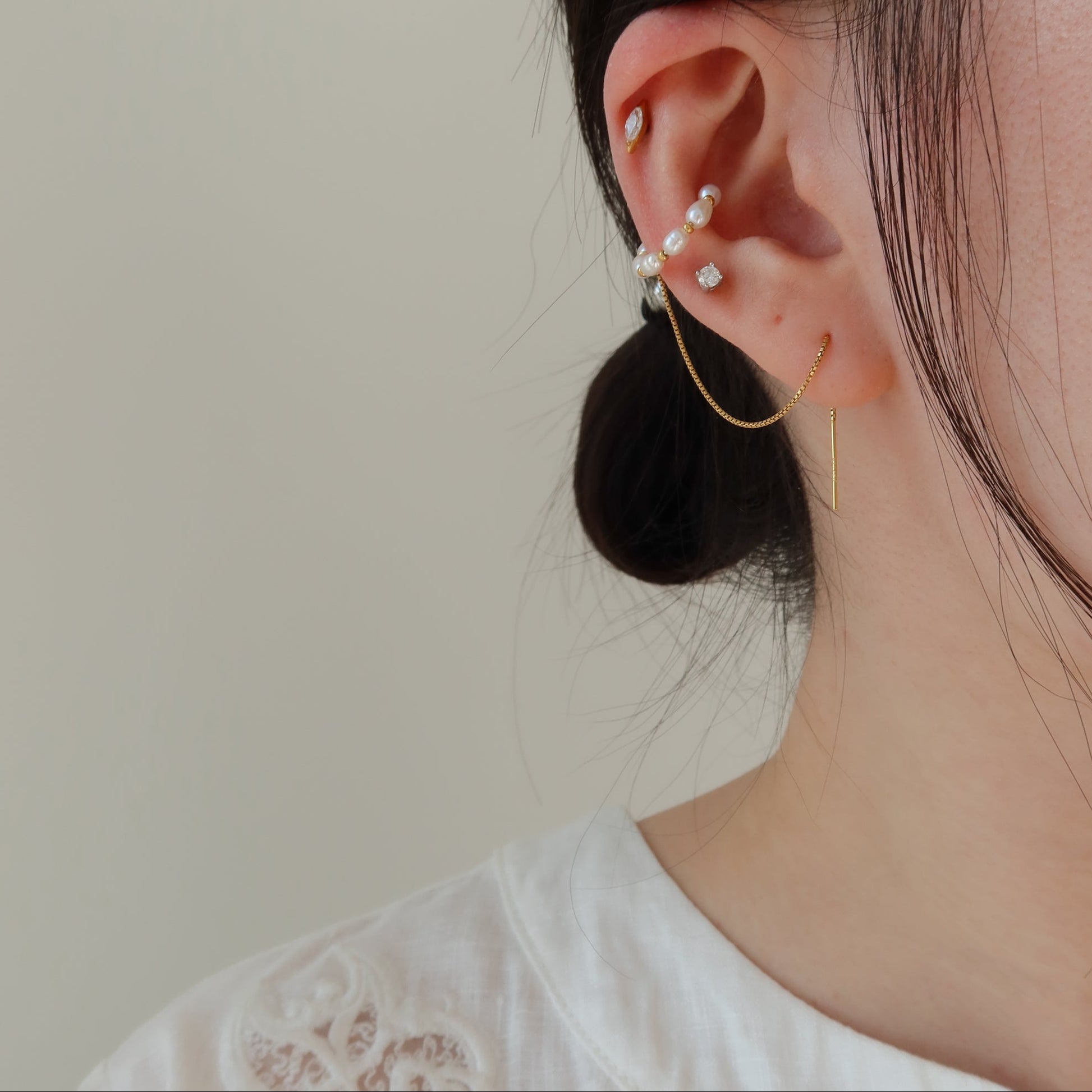 Close-up of an ear with pearl earrings against a neutral background