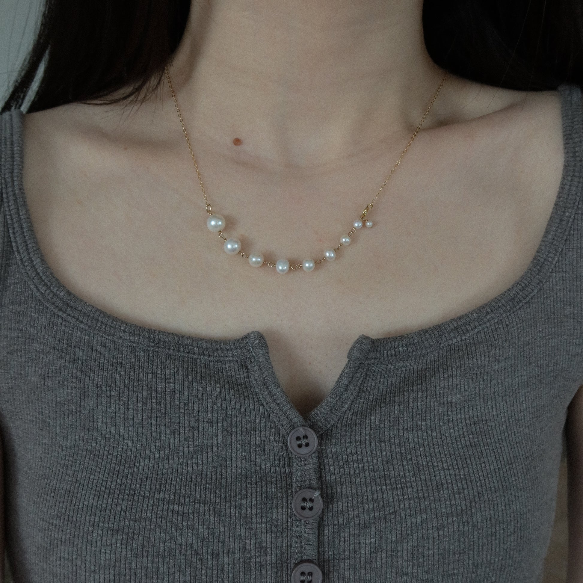 Pearl necklace worn by a person in a gray top
