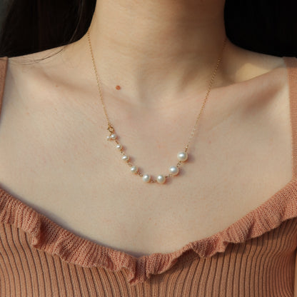 Pearl necklace on a person wearing a brown top against a black background