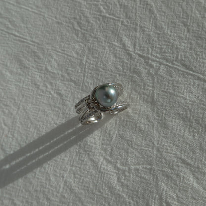 Sirene Tahitian Pearl Ring resting on a textured white surface in natural sunlight, highlighting its 8.7mm platinum-gray Tahitian pearl and twisted pavé silver band.
