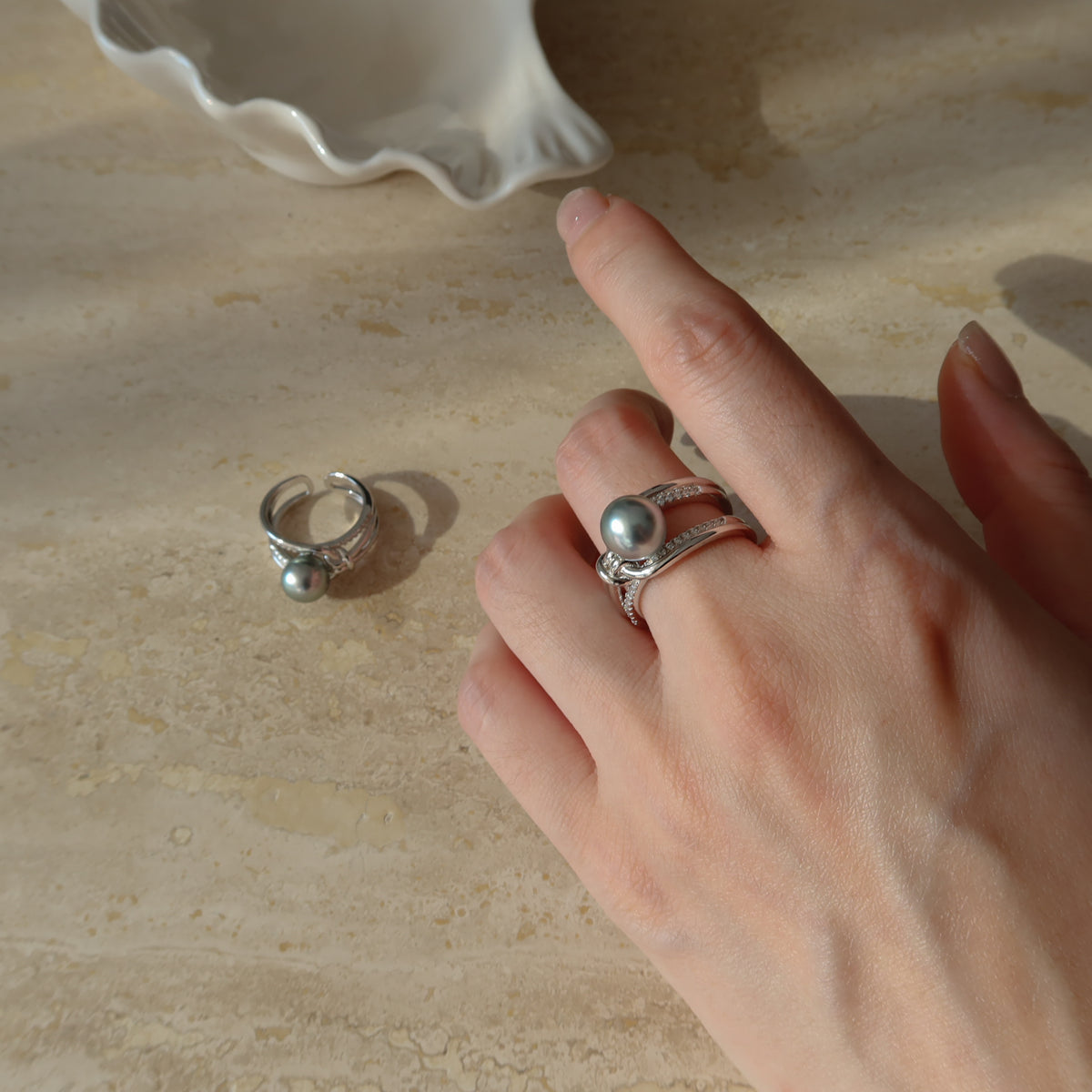 Hand wearing the Sirene Tahitian Pearl Ring featuring an 8.7mm platinum-gray Tahitian pearl and a twisted pavé silver band, with a second ring resting in the background.
