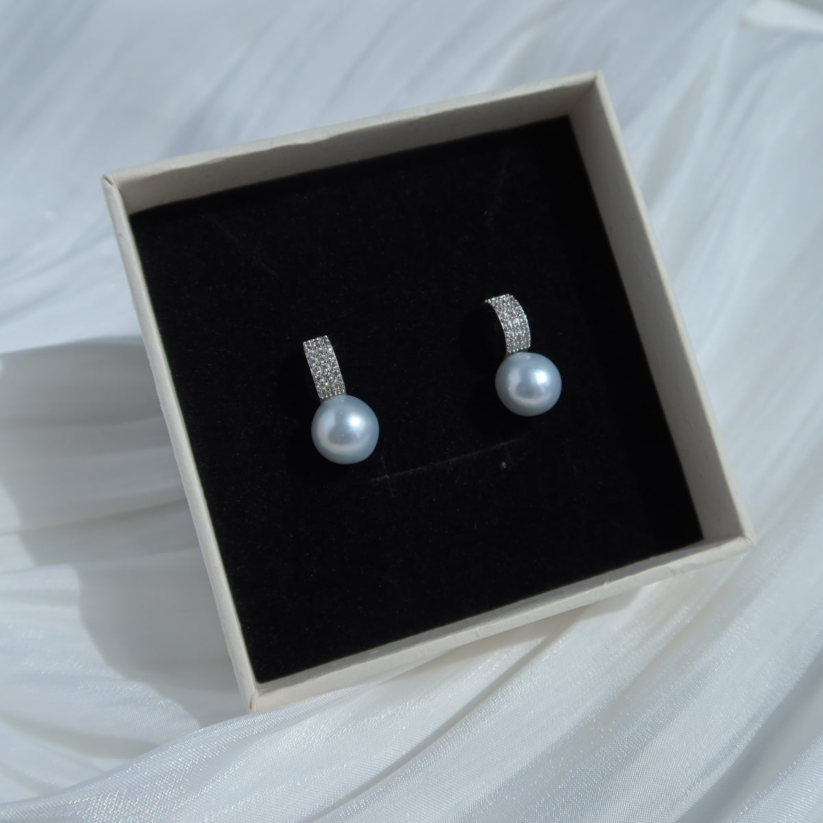 Nova South Sea Baroque Pearl Earrings resting in a presentation box, featuring blue-toned white baroque pearls and pavé huggie hoops.