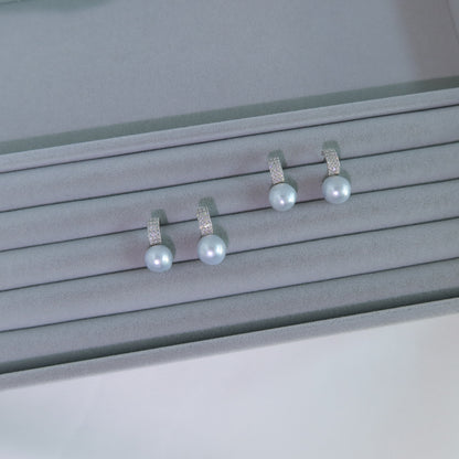 Two pairs of Nova South Sea Baroque Pearl Earrings resting on a grey velvet jewelry tray, showcasing their blue-toned white pearls and pavé huggie hoops.