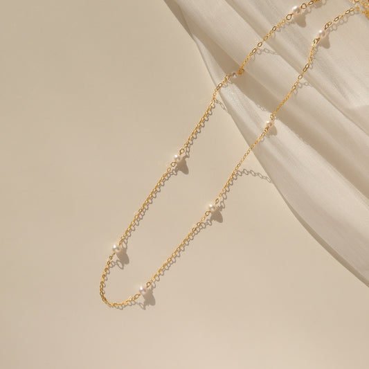 A dainty choker necklace featuring freshwater pearls on a gold-filled chain, displayed on a neutral background.